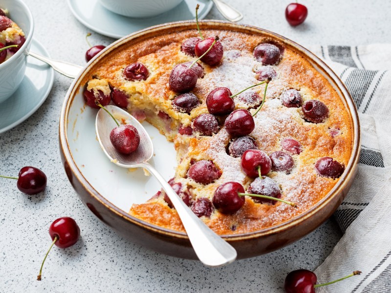 Clafoutis mit Kirschen in runder Form, in der schon eine Portion fehlt.