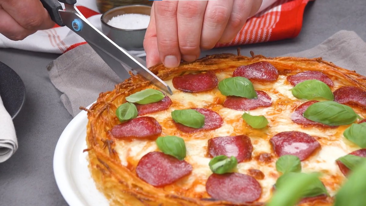 Spaghetti-Bolognese-Pizza wird mit Schere geschnitten.