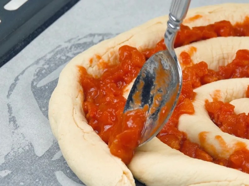 Pizzaspirale wird mit Tomatensoße bestrichen