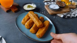 5 gefüllte Kartoffelsticks auf einem Teller und Dip in Schale im Hintergrund.