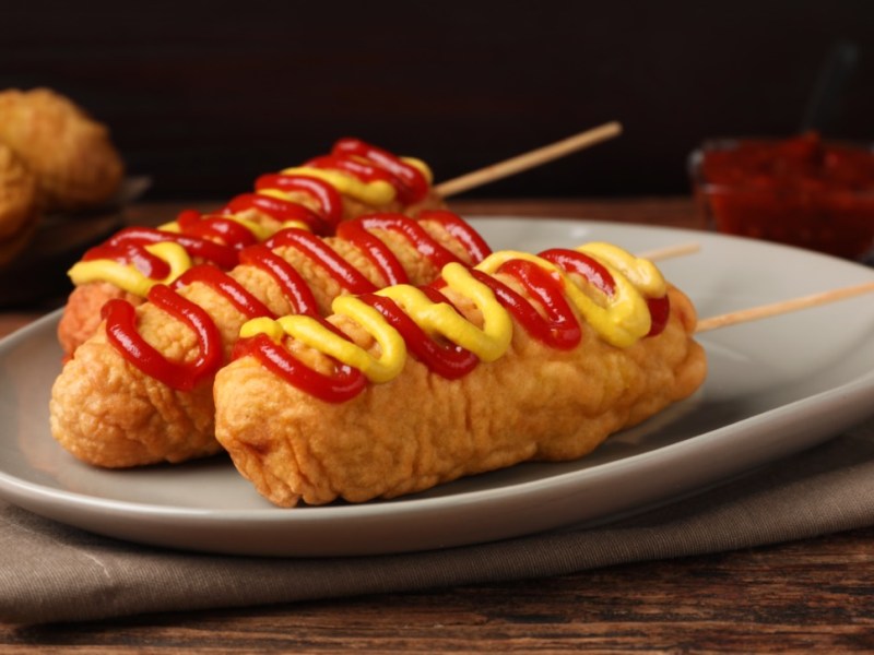 3 Corn Dogs mit Senf und Ketchup auf einem Teller.