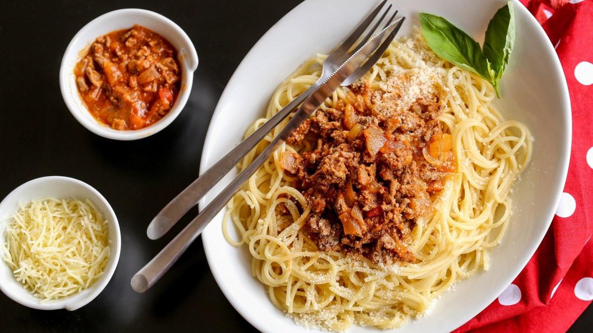 Teller mit One-Pot-Pasta à la bolognese auf holzigem Untergrund