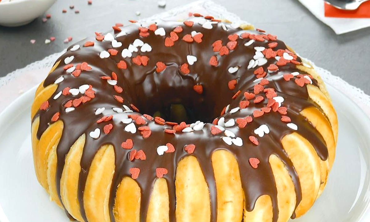 Donut-Kuchen aus 16 Teigkringeln, verziert mit Schokolade und bunten Streuseln. Serviert auf einem Teller.