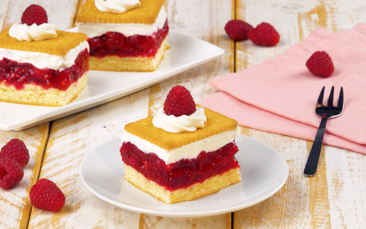 Ein StÃ¼ck Himbeer-Keks-Kuchen auf einem Teller, im Hintergrund 2 weitere StÃ¼cke