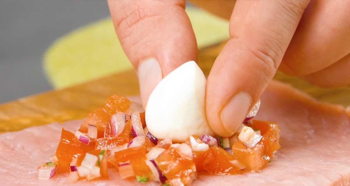 Eine kleine Mozzarellakugel wird in der Mitte der Bruschetta auf dem Schnitzel platziert