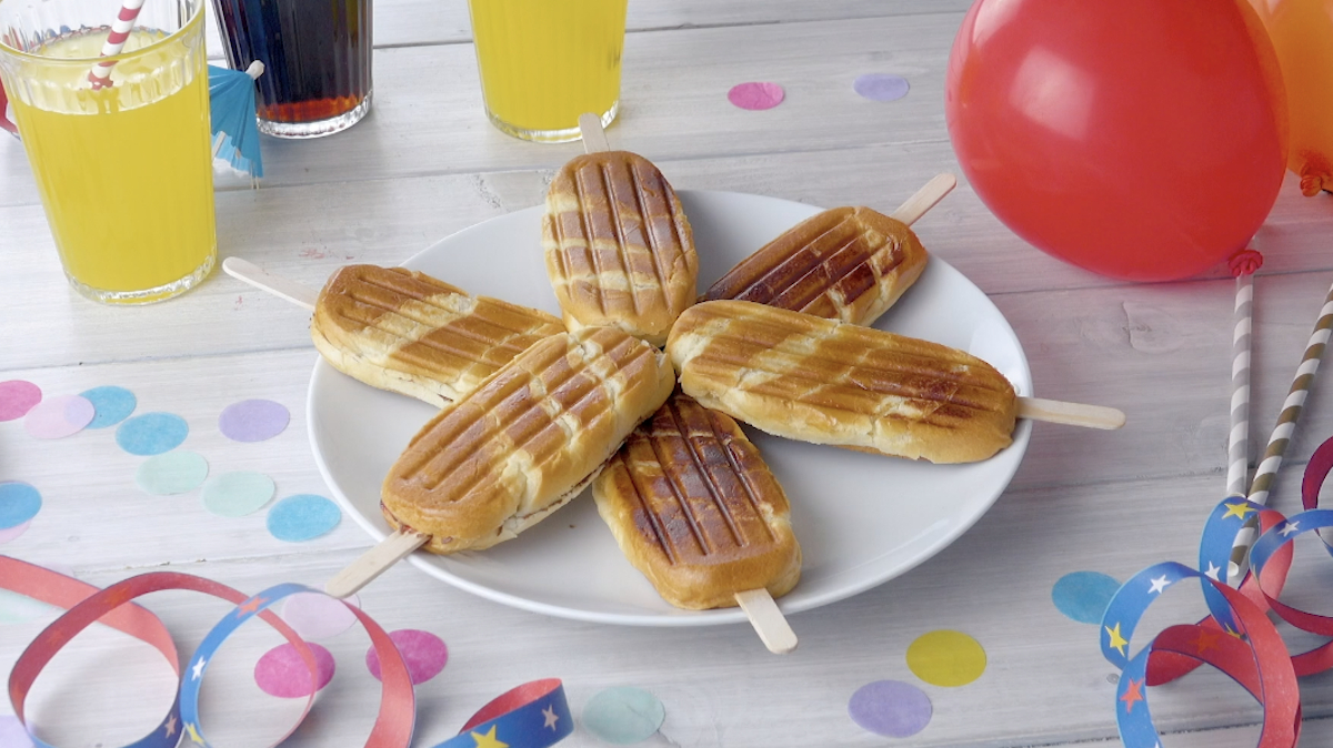 6 Milchbrötchen am Stiel, die sternförmig auf einem Teller angeordnet sind. Daneben Gläser mit Limonade, Partydekorationen und Luftballons.