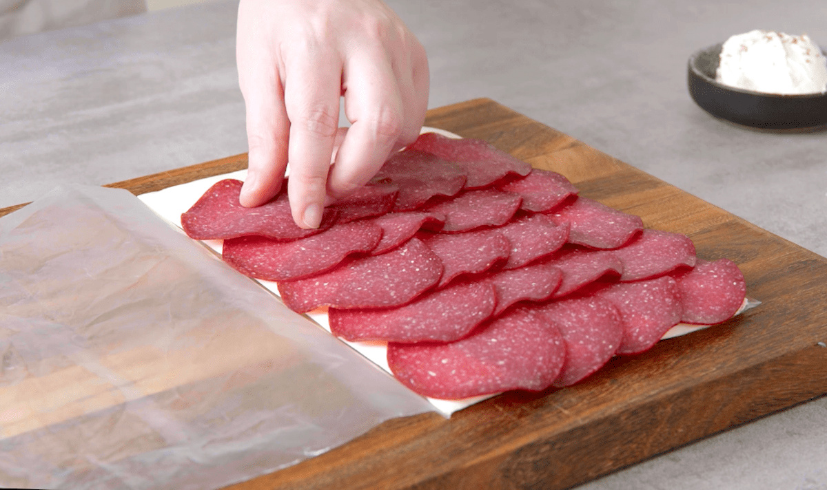 Salami Scheiben werden auf platt gerolltem FrischkÃ¤se verteilt