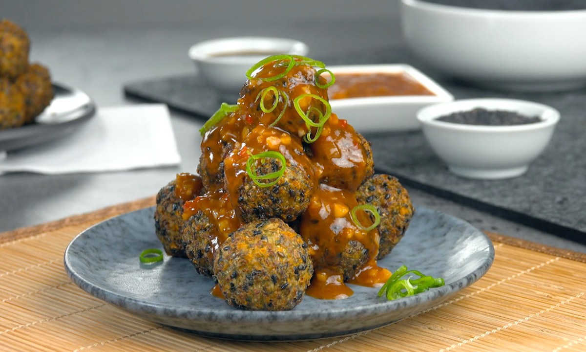 Eine Pyramide aus frittierten Gemüsebällchen mit Spitzkohl und schwarzen Sesamauf einem Teller.