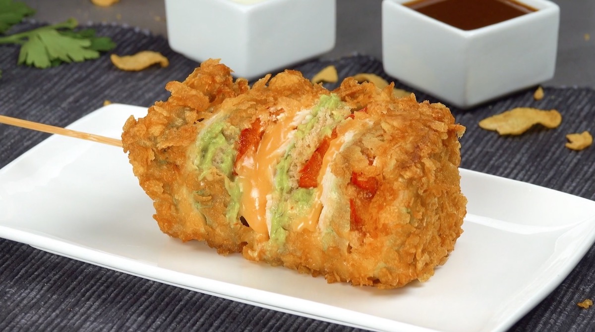 Ein Avocado-Hähnchen-Spieß auf einem Teller mit 2 Schalen mit Soße im Hintergrund.