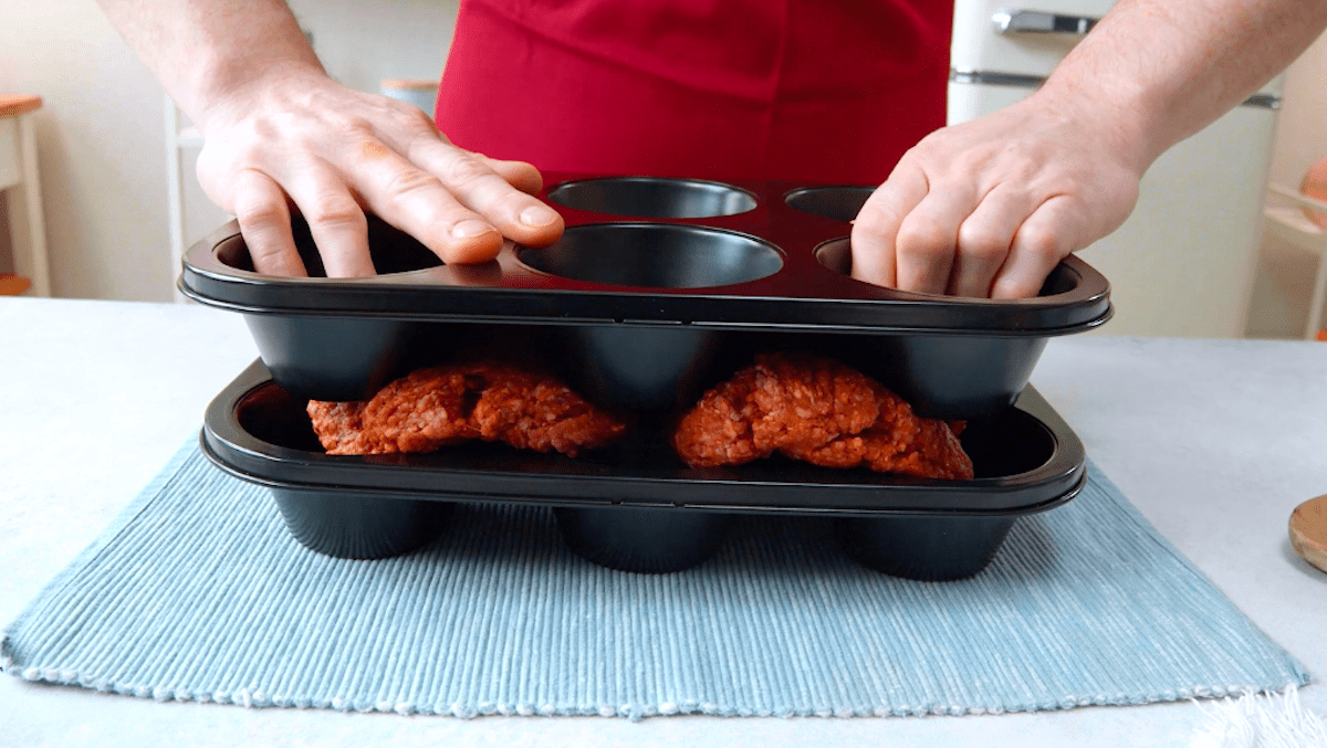 Hackfleisch wird zwischen zwei Muffinformen gepresst.