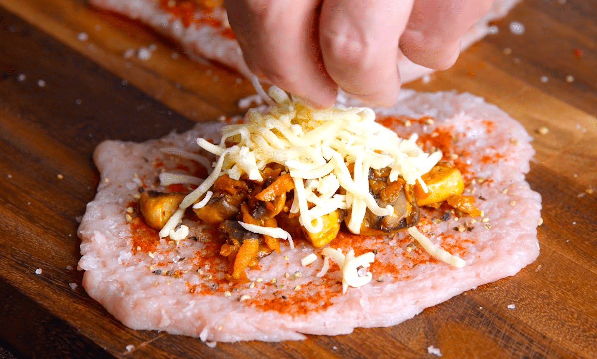 Gebratenes GemÃ¼se und geriebener KÃ¤se werden auf geplÃ¤ttetem Schweinefleisch Fleisch verteilt.