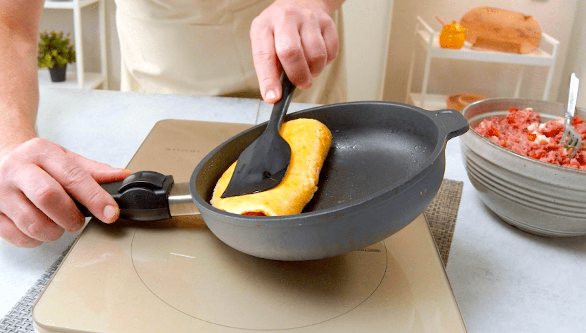 Ein halbseitig mit Hackfleisch belegter Kartoffelpuffer wird in einer Pfanne zusammengeklappt.