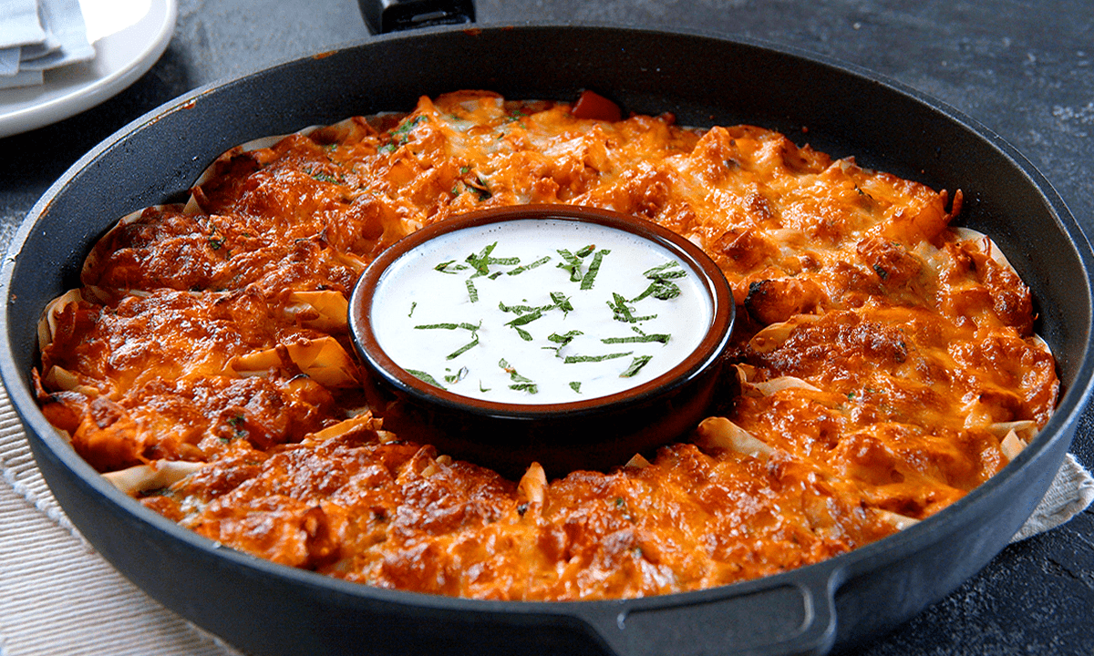 Mit Hähnchen gefüllte Teigtaschen in einer Form, ein Schälchen mit Dip steht in der Mitte.