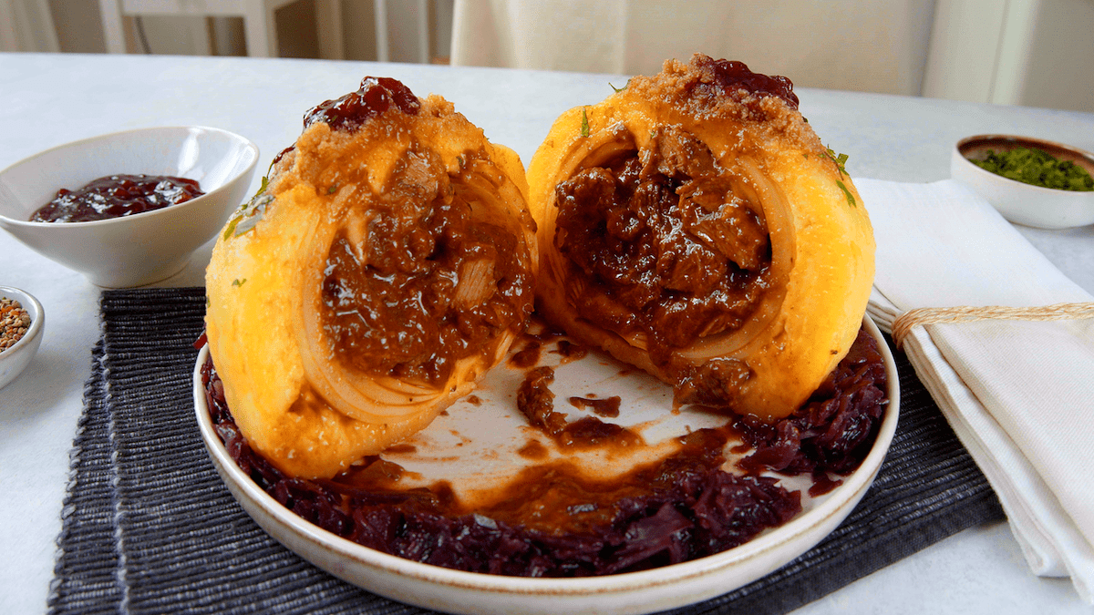 Eine mit Rinderragout gefÃ¼llte Zwiebel in KloÃŸteig auf Rotkohl mit Semmelbutter