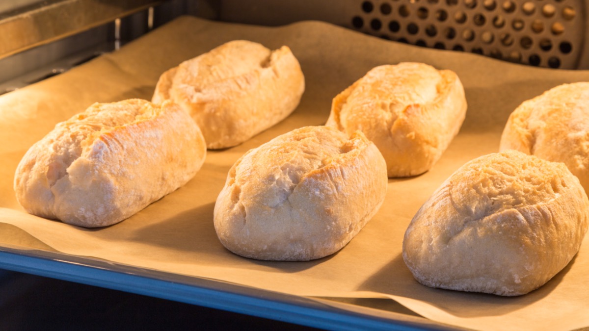 Brötchen auf einem mit Backpapier belegten Backblech im Ofen.