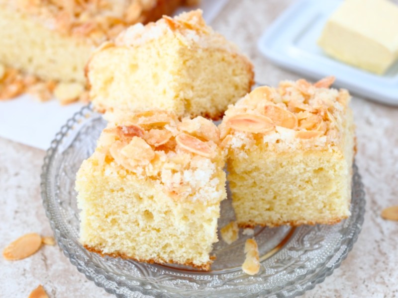 Mehrere Stücke Butterkuchen mit Mandeln auf einem Glasteller.