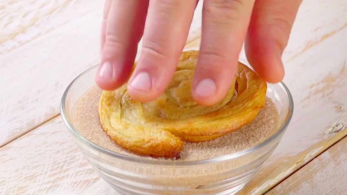 Gebackene Churroplattte wird in Zucker-Zimt-Mischung getaucht