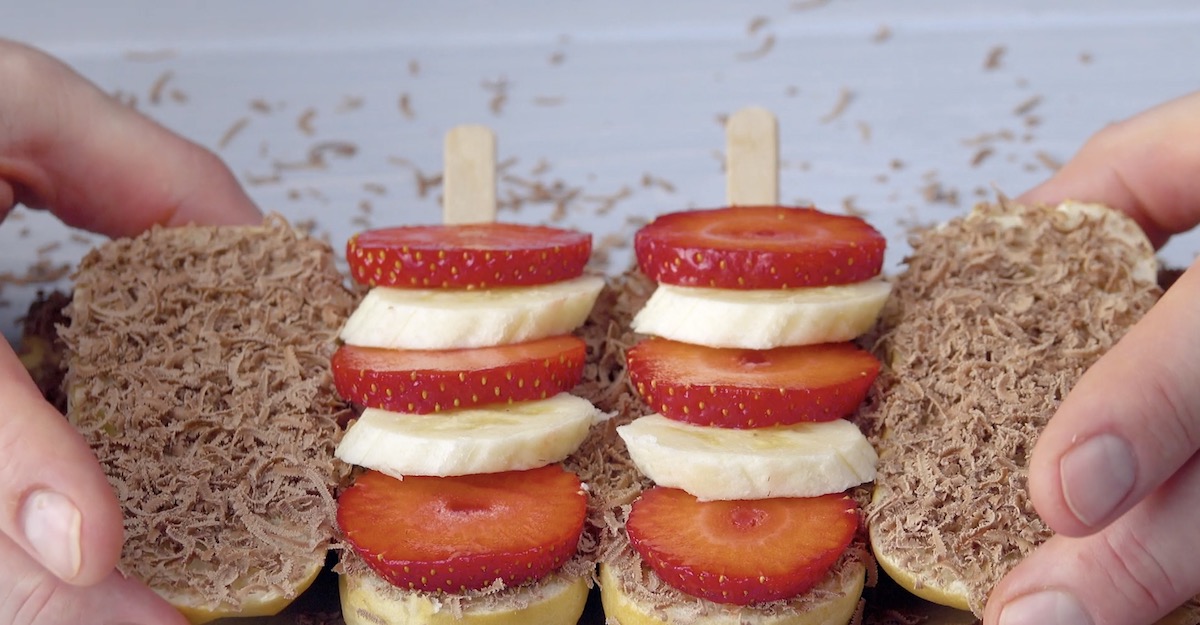 Erdbeer- und Bananenscheiben werden abwechselnd auf die MilchbrÃ¶tchen mit Stiel gelegt.