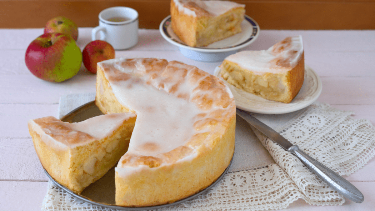 Ein gedeckter Apfelkuchen, aus dem mehrere Stücke entnommen wurden, daneben eine Tasse Kaffee und die Stücke auf Tellern