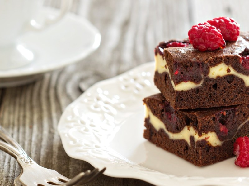 Zwei Himbeer-Cheesecake-Brownies übereinander auf einem Teller.