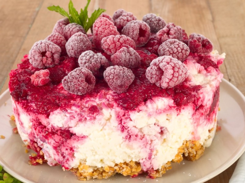 Eine Himbeerschnitte ohne Backen auf einem Teller mit Himbeeren als Garnitur.