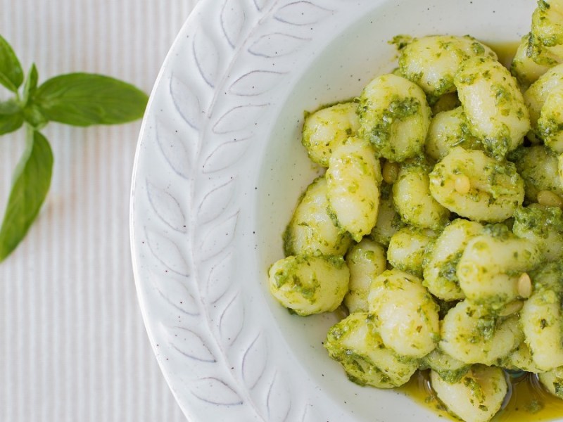 Ein Teller Low-Carb-Gnoochi mit Basilikumpesto. Daneben liegt frischer Basilikum.