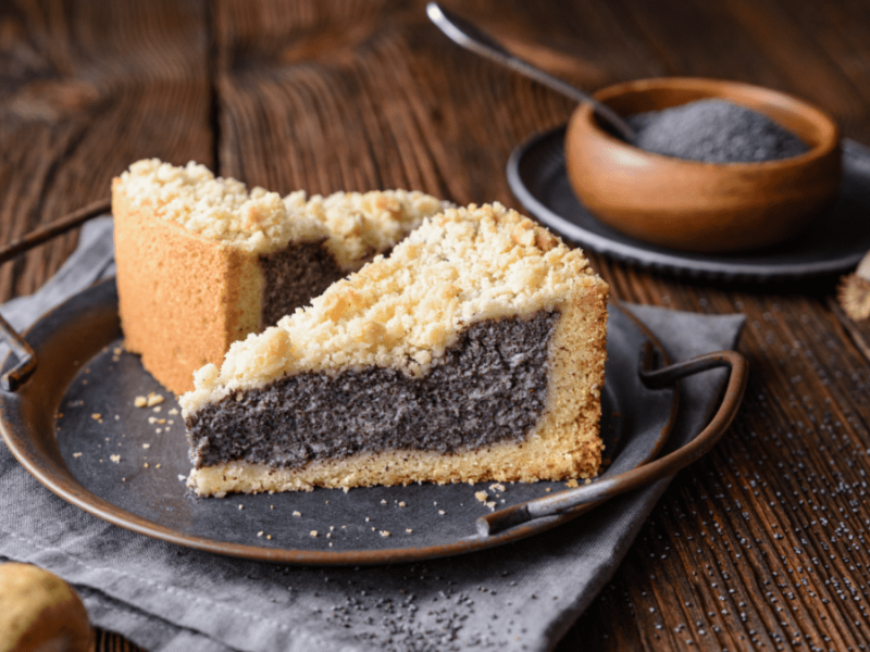 Zwei Stücke Mohnkuchen mit Streuseln auf einem Teller, daneben eine Schale mit Mohnkörnern