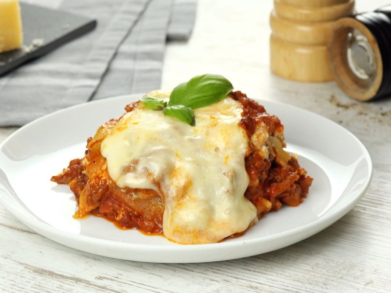 Eine Portion One-Pot-Lasagne auf einem Teller, im Hintergrund Pfeffer- und Salzmühle.