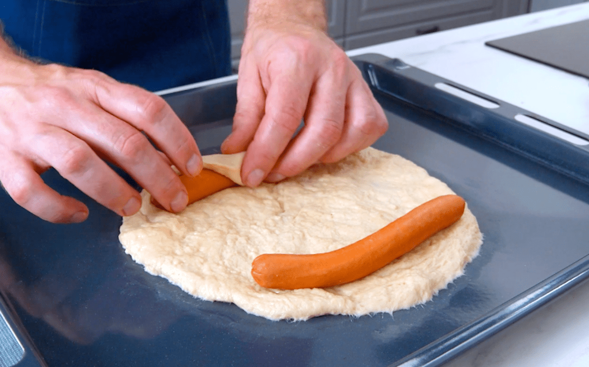 Zwei WÃ¼rstchen liegen auf einem ausgerollten StÃ¼ck Hefeteig