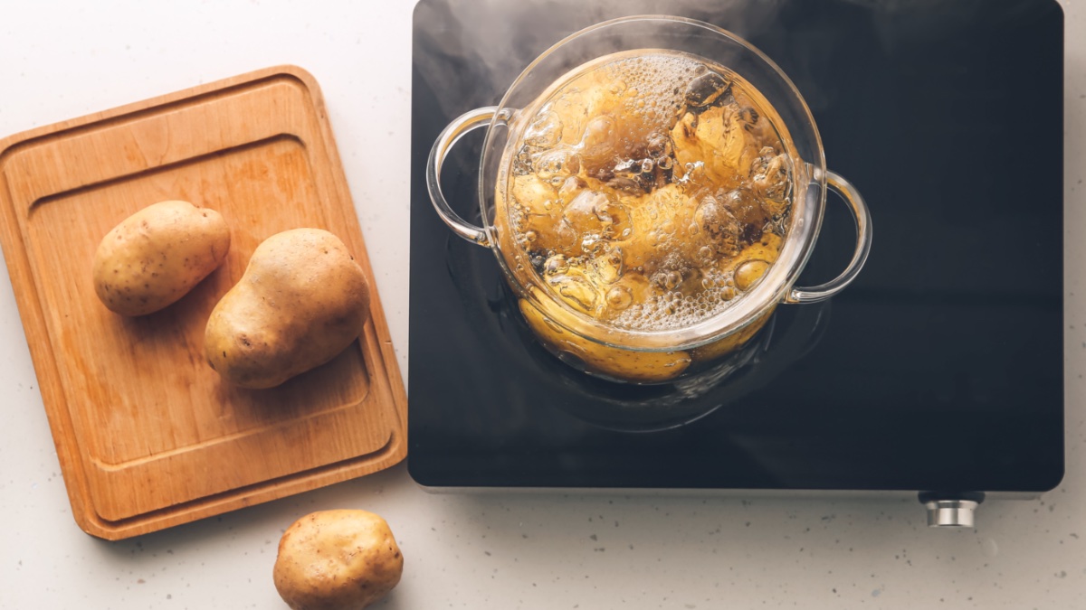 Salzkartoffeln kochen in einem Topf in der Draufsicht, daneben ein Brett mit Kartoffeln.