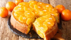 Ein Schüttelkuchen mit Mandarine. Ein großes Stück wurde herausgeschnitten und liegt vor dem Kuchen.