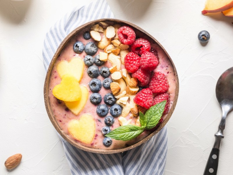 Ein bunte Smoothie-Bowl mit Porridge. Daneben liegen ein Löffel und frische Zutaten.