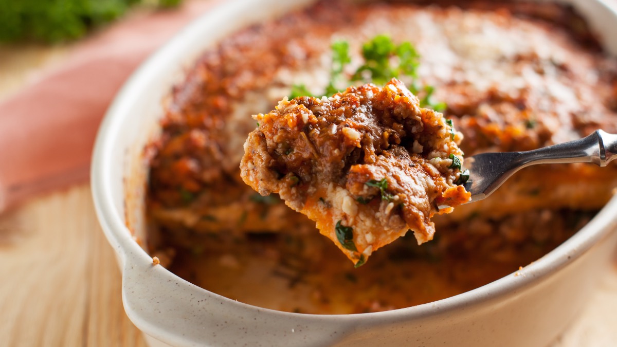 Eine Portion Süßkartoffel-Lasagne wird mit einer Gabel aus der auflauffrom entnommen.