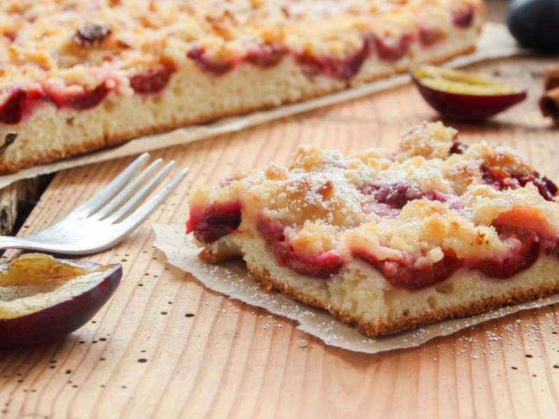 Ein Stück Zwetschgen-Streuselkuchen vor dem ganzen Kuchen.