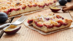 Ein Stück Zwetschgen-Streuselkuchen vor dem ganzen Kuchen.