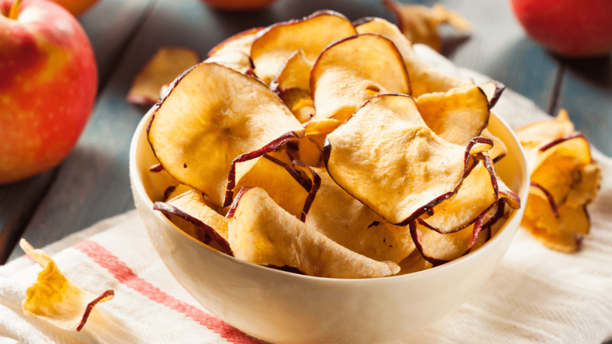 Eine Schale voller Apfelchips. Im Hintergrund frische Äpfel.