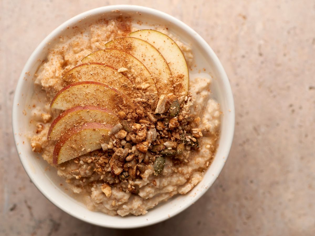 Apfelstrudel-Porridge, angerichtet in einer weißen Schüssel, getoppt mit Apfelscheiben, Walnüssen und Zimt