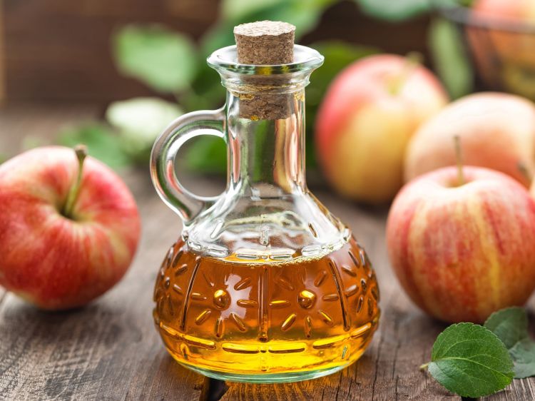 Bratapfel-Likör in einer bauchigen Flasche, im Hintergrund liegen Äpfel.