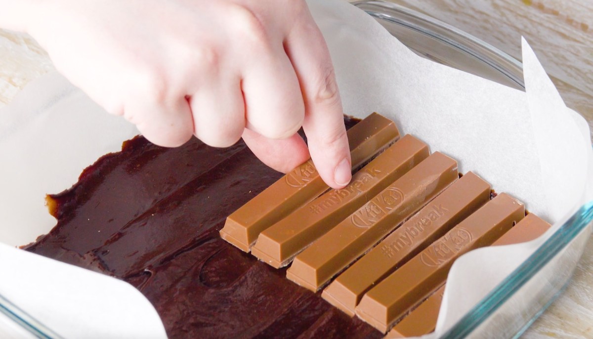 Ein noch ungebackener Kit-Kat-Kuchen in der Auflaufform, auf den gerade Schokoriegel gelegt werden.