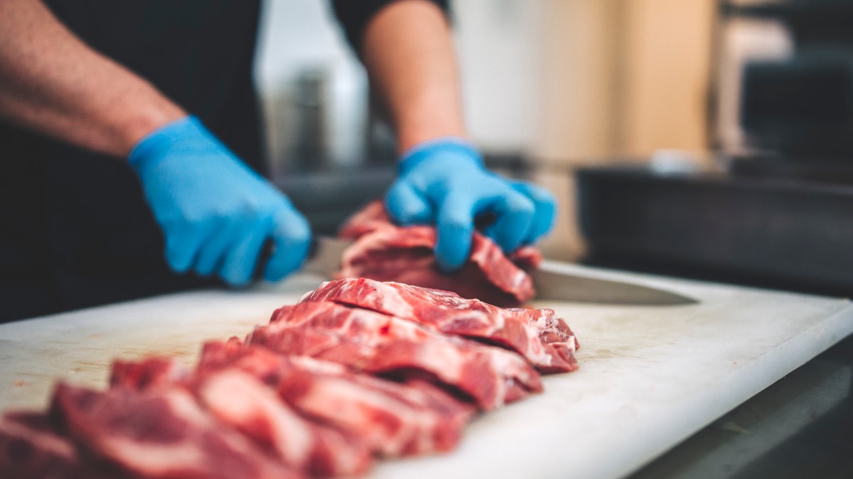 Mann mit blauen Handschuhen schneidet Fleisch