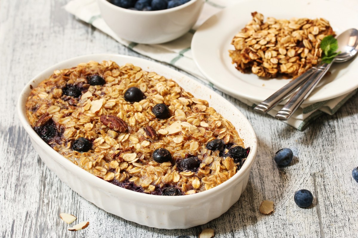 Eine Auflaufform mit gebackenen Blaubeer-Bananen-Haferflocken und Nüssen, daneben ein Teller mit einer Portion.