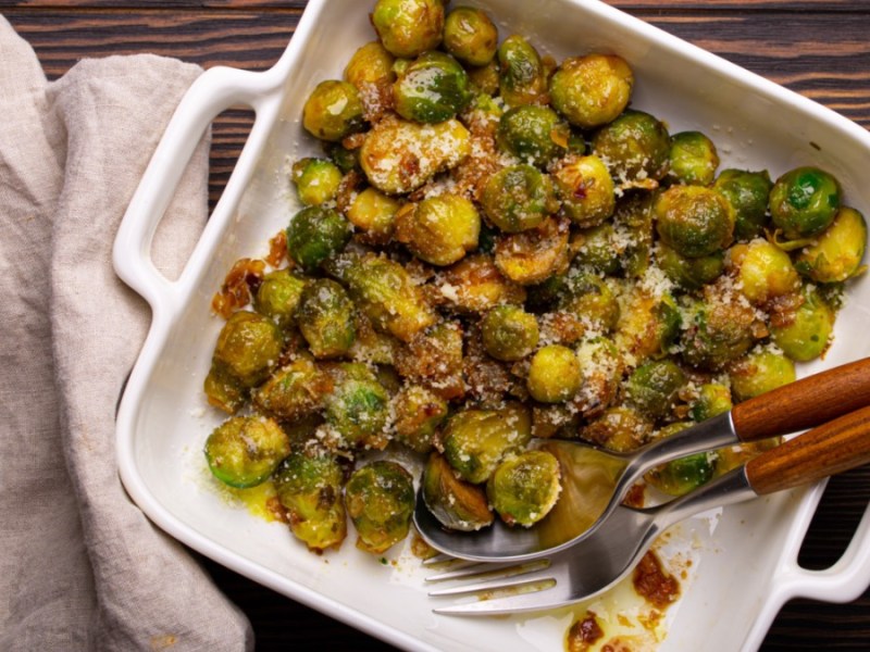 Gebratener Rosenkohl mit Parmesan in Auflaufform, daneben ein Geschirrtuch.