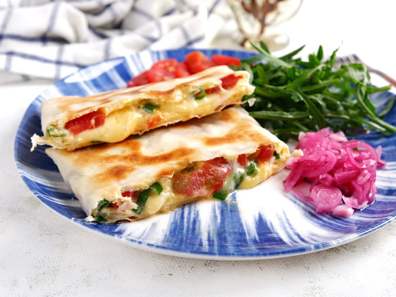 2 getoastete Wraps mit Avocado und Tomaten auf einem blau-weiß gemusterten Teller, darauf auch eingelegtes Gemüse.