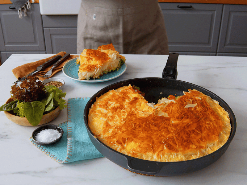 Eine herbstliche Börek-Pfanne mit Kürbis und Yufka-Teig auf einer Küchentheke, daneben eine Schale Salz und ein Teller mit einem Stück des Auflaufes.