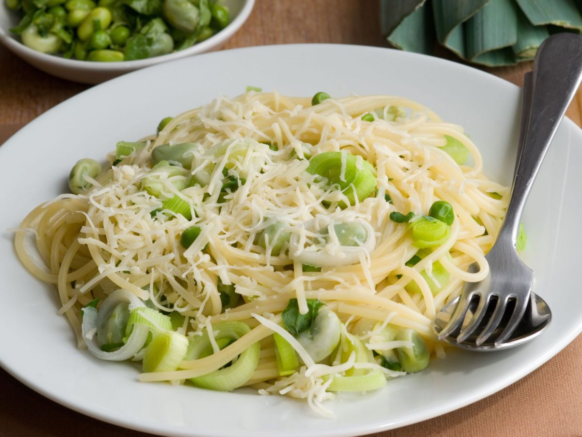 Käse-Lauch-Pasta mit viel Käse, serviert auf einem Teller. Daneben liegen Gabel und Löffel.