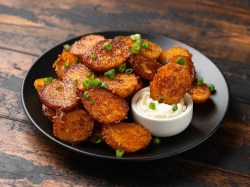 Parmesan-Kartoffeln mit Frühlingszwiebeln bestreut auf einem schwarzen Teller, auf dem auch eine Schale mit weißem Dip steht.