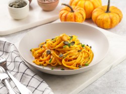 Ein Teller Pasta mit Kürbis und Feta, daneben Kürbisse und ein kariertes Geschirrtuch.