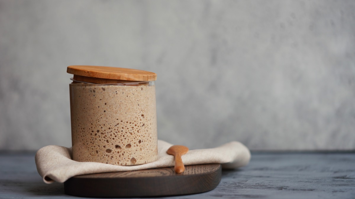 Ein Glas mit Sauerteig auf einem Tuch und einem Holzbrett