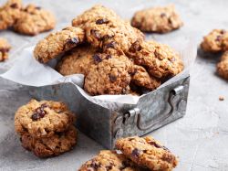 Haferflocken-Cookies in einer Keksdose, daneben liegen noch mehr Kekse.