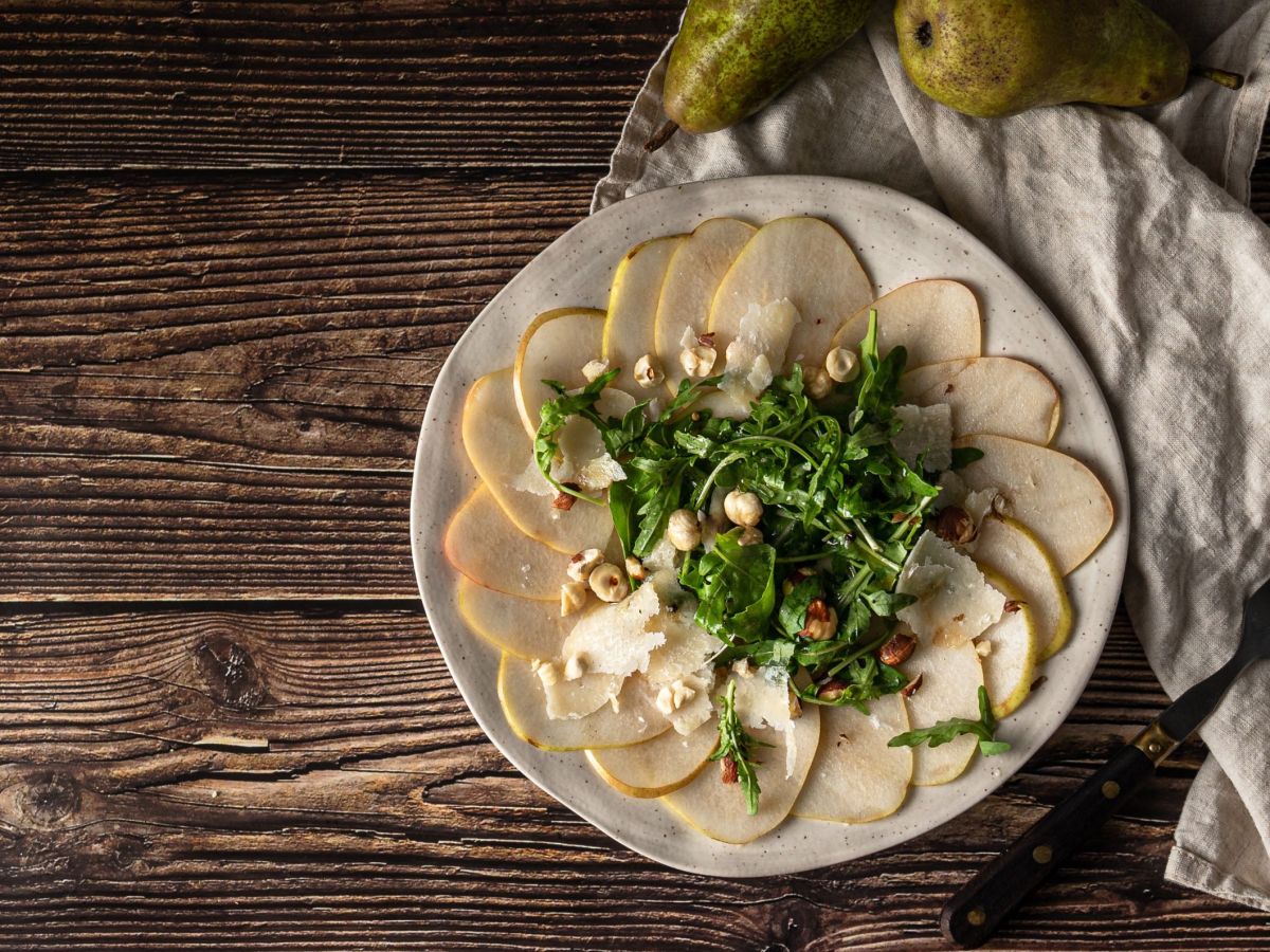 Birnen-Carpaccio mit Gorgonzola und WalnÃ¼ssen arrangiert auf einem Teller. Eine helle Tischdecke liegt daneben.